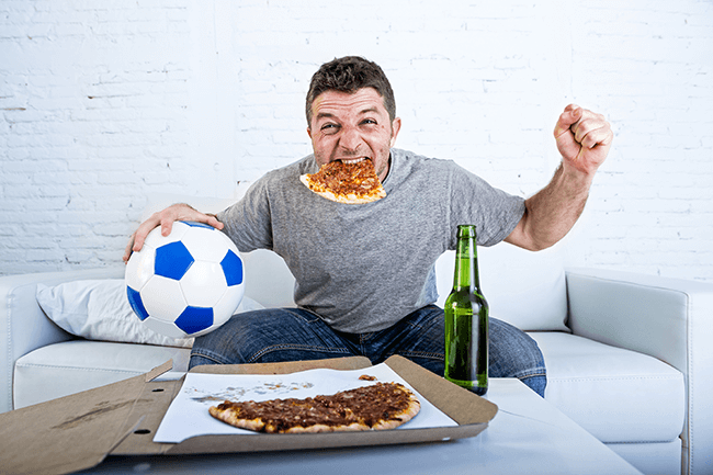 Guy eating pizza, drinking beer and watching soccer.